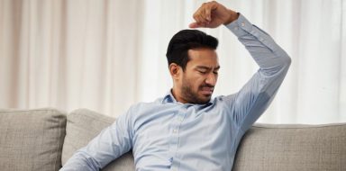 A man sitting on a couch, looking at his underarm sweat.