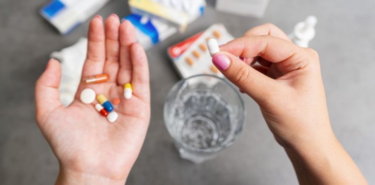 A close up of a woman's hands. She is holding an assortment of pills.