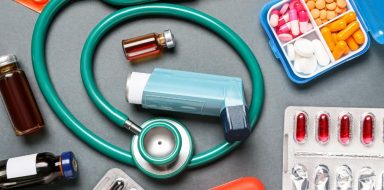 An inhaler, pills, and stethoscope on a table.