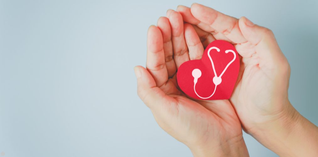 Two hands holding a paper heart, with a drawing of a stethoscope.