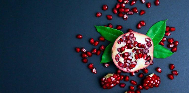 A pomegranate cut in half, with some of the seeds out on a black surface.