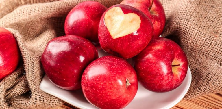A plate covered in red apples. One of them has the shape of a heart cut into it.